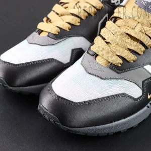 Close-up of Nike Air Max 1 “Low Poly - Big Head Mode” toe box highlighting contrast between black-grey panels and gold laces.