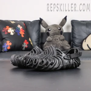 The Salehe Bembury x Crocs Pollex Clog “Sasquatch” delivers a bold, monochromatic take on the iconic silhouette, combining sculptural design with all-day comfort performance. Constructed with a fully blacked-out Croslite™ foam upper, this model showcases flowing concave ridges inspired by Salehe Bembury’s signature fingerprint motif, creating a futuristic and organic visual identity. The textured design not only enhances aesthetics but also improves structure and flexibility. Strategically placed ventilation ports promote airflow, ensuring breathable wear throughout the day. Built for functionality, the clog features an adjustable nylon heel strap for a secure and customizable fit, while dual Crocs and Salehe Bembury branding appears on the contoured footbed. Underfoot, durable rubber pods are placed in high-wear areas of the outsole, delivering enhanced traction and stability across various surfaces. Key Features: • Croslite™ foam construction for lightweight comfort and cushioning • All-black “Sasquatch” colorway for a sleek, versatile look • Signature fingerprint-inspired ridges for bold sculptural design • Ventilation ports for enhanced breathability • Adjustable nylon heel strap for a secure fit • Dual Crocs x Salehe Bembury branding for authenticity • Rubber outsole pods for improved traction and durability The “Sasquatch” Pollex Clog is perfect for those who want a minimal yet statement-making comfort shoe, blending avant-garde aesthetics with everyday practicality.