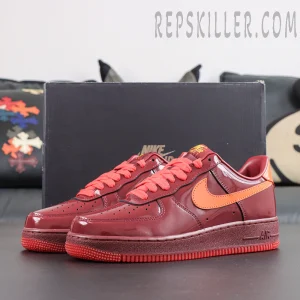 Nike Air Force 1 Low ‘Patent Leather Dark Team Red’ pair display featuring dark red patent leather, orange accents and an all-red outsole